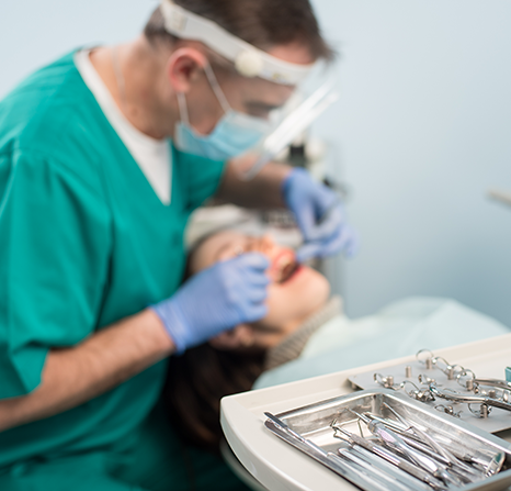 A table with dental tools in focus while a dentist works in the blurred background.